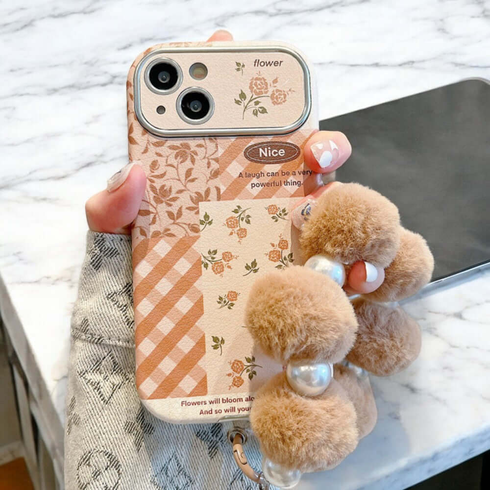 a person holding a phone case with two pom poms attached to it